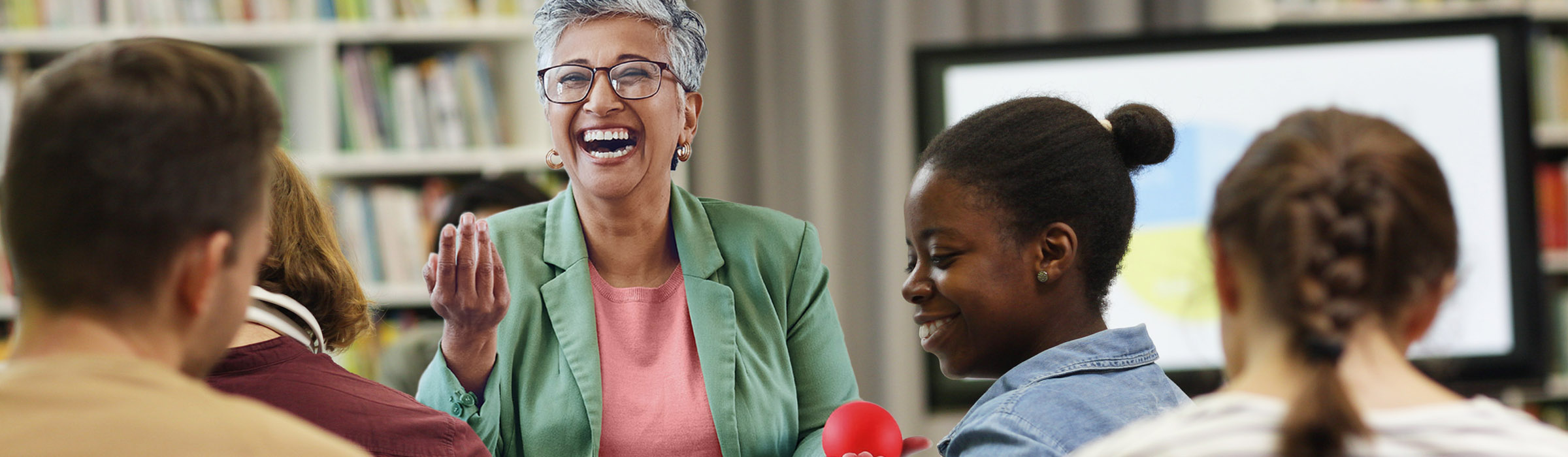 Eine Lehrerin steht lachend vor einer Klasse.